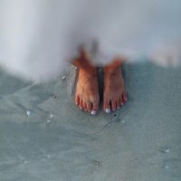 Top view of a woman's bare feet on wet sandy beach at seashore.